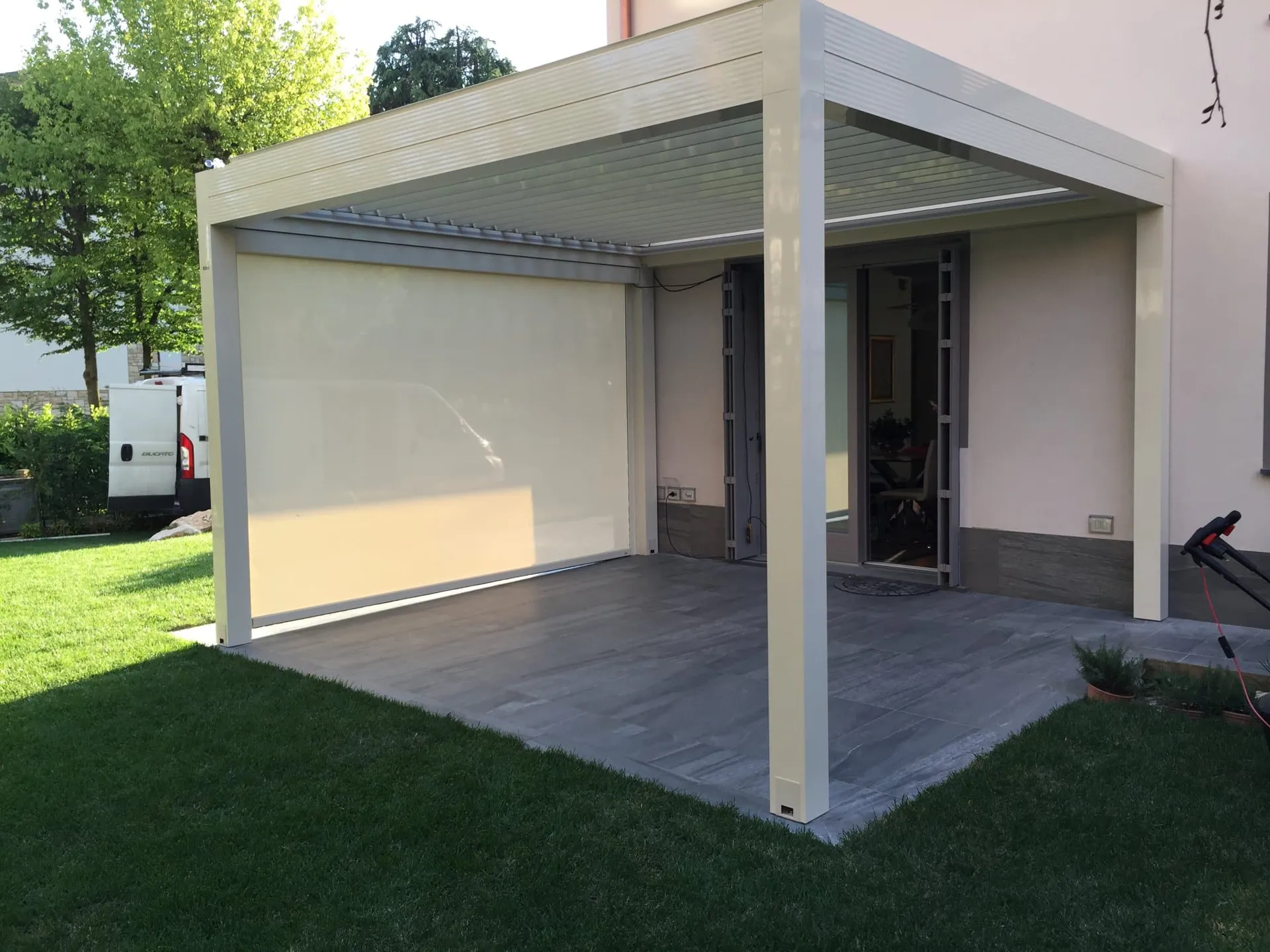 Pergola bioclimatica bianca con telo laterale abbassato su un prato